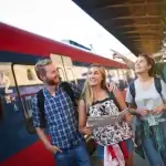 Jovens estudantes olhando as rotas de trem em um mapa com o trem ao lado.