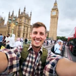 Jovem sorrindo ao tirar uma selfie em Londres, ilustrando a experiência de um intercâmbio para conhecer as curiosidades da Inglaterra.