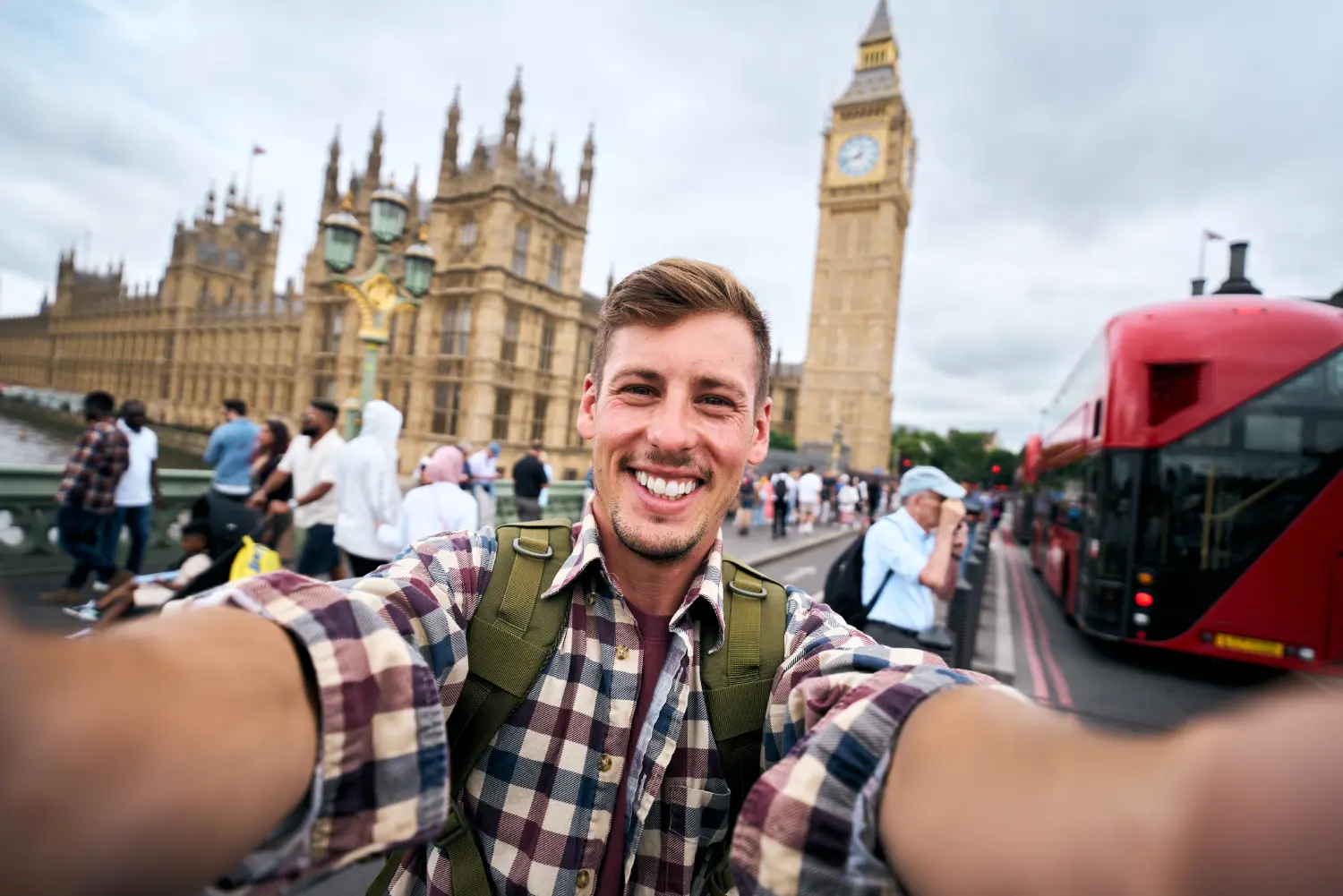 Jovem sorrindo ao tirar uma selfie em Londres, ilustrando a experiência de um intercâmbio para conhecer as curiosidades da Inglaterra.