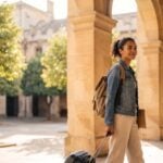 Estudante brasileira com mochila e mala caminhando pelo pátio de uma universidade europeia, representando a faculdade multicampi em 4 países